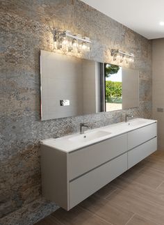 a bathroom with two sinks, mirrors and lights on the wall above them is shown