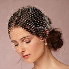 a woman wearing a birdcage veil with pearls on her head and hair comb