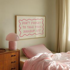 a bedroom with pink bedding and a framed sign on the wall above it that says don't forget to take your makeup off