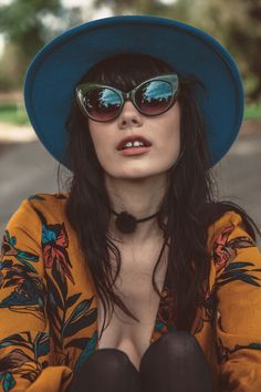 a woman wearing sunglasses and a hat with her hands on her hips while sitting down