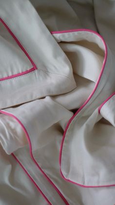 an unmade bed with white sheets and pink piping on the edges, along with two pillows