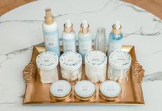 an assortment of personal care products displayed on a gold tray in front of a marble table