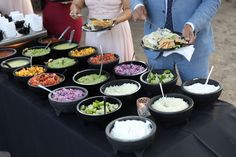 a man and woman standing next to a table filled with bowls full of different foods