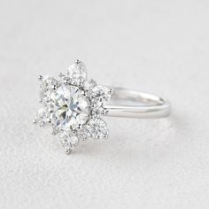 an engagement ring with a flower shaped center surrounded by round brilliant cut diamonds on a white background