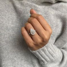 a woman's hand with a diamond ring on her finger, wearing a gray sweater