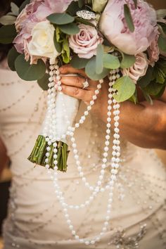 a woman in a wedding dress holding a bouquet with pearls and flowers on her arm