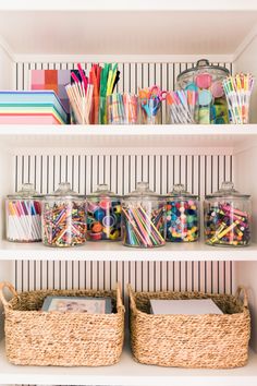 organized craft supplies in glass jars on shelves with striped wall paper and straw baskets below