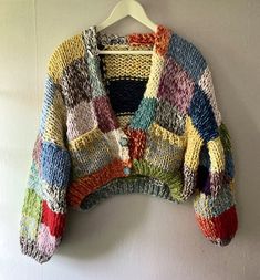 a multicolored sweater hanging on a white wall with a hanger in front of it