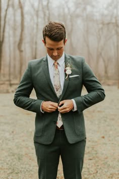 a man in a suit and tie is looking down at his pocket while wearing a boutonniere