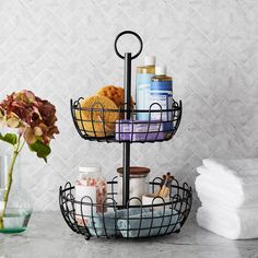 three tiered metal basket with various items in it on a counter next to a vase