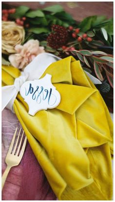 a yellow napkin with a name on it next to a fork and flower bouquets