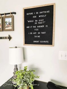 a desk with a lamp, potted plant and a framed sign on the wall