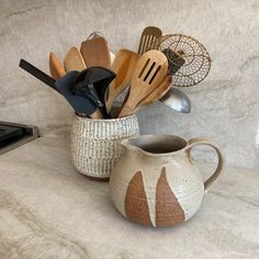 a ceramic pitcher with spoons and utensils in it sitting on a counter