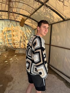 a young man standing in front of a building wearing a crocheted sweater and black shorts