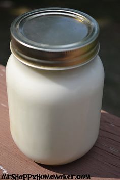 a glass jar filled with white liquid sitting on top of a wooden table next to water