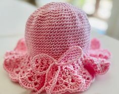 a crocheted pink hat with a bow on the front and side, sitting on top of a white table