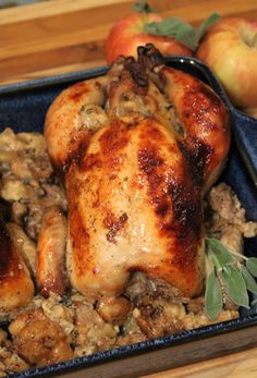 a close up of a chicken in a pan on a table with apples and leaves