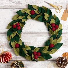 a christmas wreath made out of felt, pine cones and holly leaves with red berries