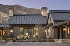 a house with stone and metal roofing in front of a mountain range at dusk