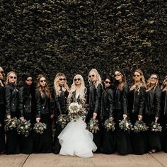 a group of women standing next to each other in front of a wall with plants