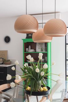 a glass table topped with a vase filled with white flowers and green bookshelves