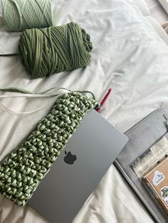 an apple laptop computer sitting on top of a bed next to yarn and knitting needles