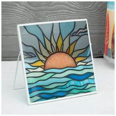 a stained glass picture frame with the sun and water on it, sitting next to a book