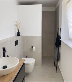 a white toilet sitting next to a bathroom sink under a window on top of a wooden counter