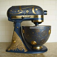 a blue mixer with gold designs on it sitting on top of a counter next to a white tile wall