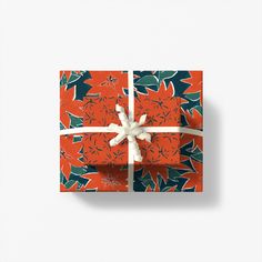 an orange gift box wrapped in red and green wrapping paper with a white bow on top