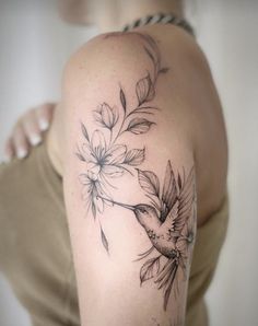 a woman's arm with flowers and a hummingbird tattoo on her left shoulder