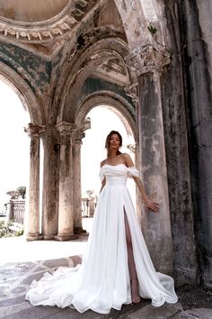 a woman in a white dress posing for a photo inside an old building with columns and arches