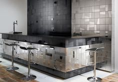 a modern kitchen with black and silver tiles on the backsplash, bar stools