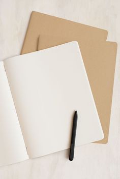 two notebooks and a pen sitting on top of each other