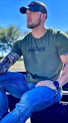 a man sitting on top of a blue truck wearing a black hat and green shirt