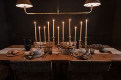 a wooden table topped with plates and bowls filled with food next to tall candles in the dark