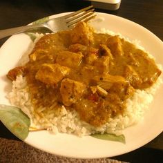 a white plate topped with rice and meat covered in gravy next to a fork