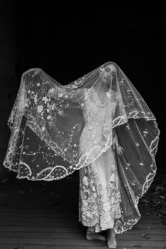 black and white photograph of woman in wedding dress with veil over her head, standing on wooden floor