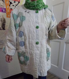 an older woman wearing a white coat and green scarf standing in front of a door