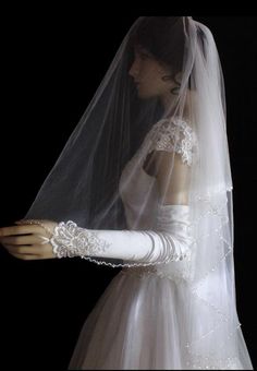 a woman wearing a wedding veil and dress with white gloves on her arm, in front of a black background