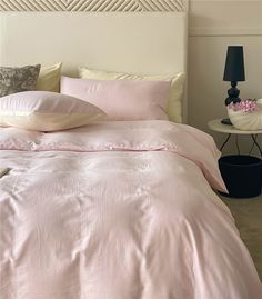 a bed with pink sheets and pillows in a bedroom next to a night stand on the floor