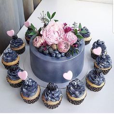 cupcakes with blue frosting and pink flowers in the shape of hearts are arranged on a white table