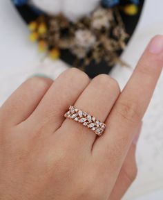 a woman's hand with a ring on her finger and flowers in the background