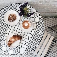 two croissants and some coffee on a white table with black geometric tiles