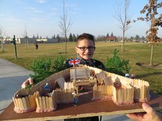 a young man holding up a model of a castle made out of wooden planks