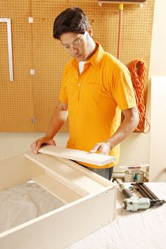 a man in an orange shirt sanding down a piece of paper on a table