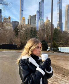 a woman standing in front of a city skyline holding a cup of coffee and looking off into the distance