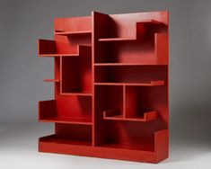 a red book shelf sitting on top of a white floor next to a gray wall