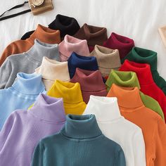 many colors of sweaters are laid out on a white sheet with a clock in the background