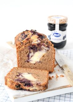 a loaf of blueberry bread on a cutting board with butter and jam in the background